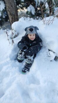mały chłopiec siedzi w zaspie śniegu