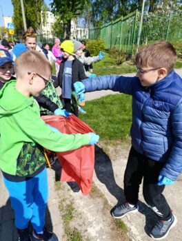 Uczniowie zbierają śmieci, chłopiec trzyma worek do którego inny wrzuca odpady