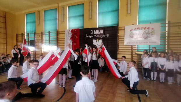 Chłopcy i dziewczęta podczas tańca rozwijają biało czerwone flagi.